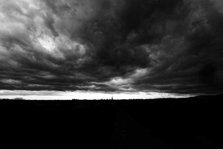 Schwarzweiß: dramatische Wolkenfront über einem Dorf mit Kirchturm